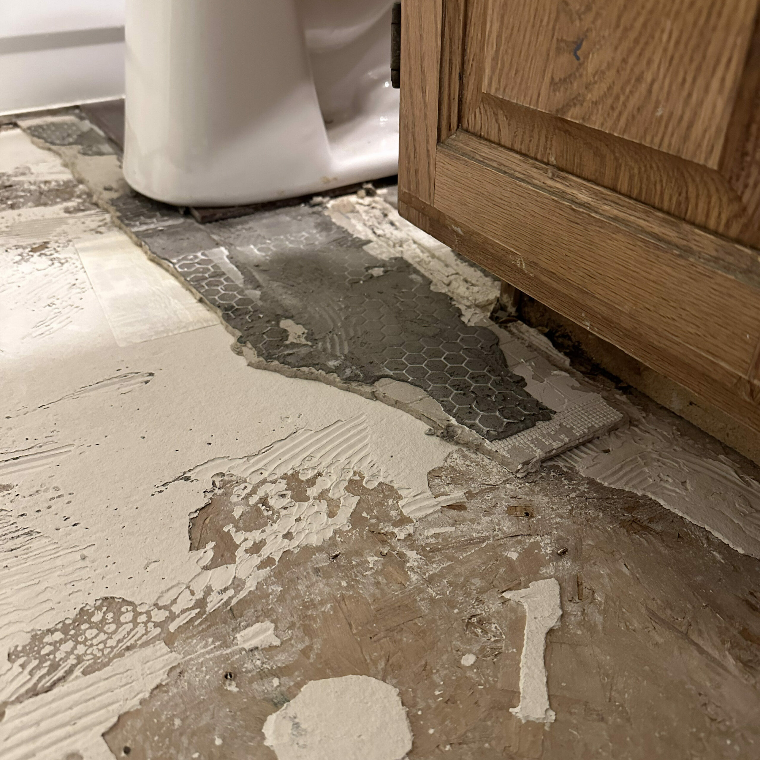 layers underneath a floor tile: subfloor, backerboard, tile, and then the toilet.