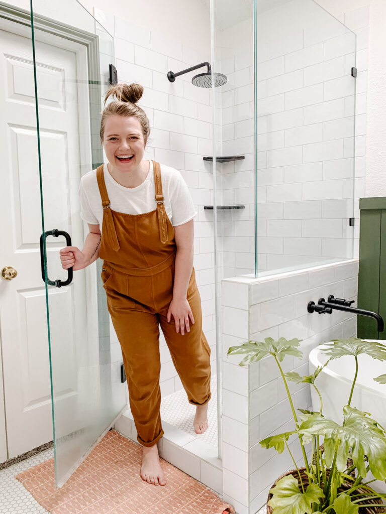 Woman standing in front of a recently remodeled shower with while tile and clear glass shower door