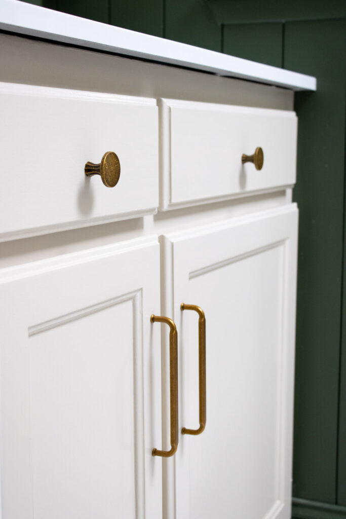 Warm gray painted bathroom cabinet with brass handles and knobs.