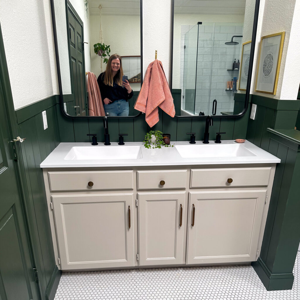 Painted bathroom cabinet after with warm gray paint and brass handles in a green and white bathroom.