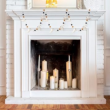 White fireplace with white candles inside and a orange and blank garland hung on the mantel