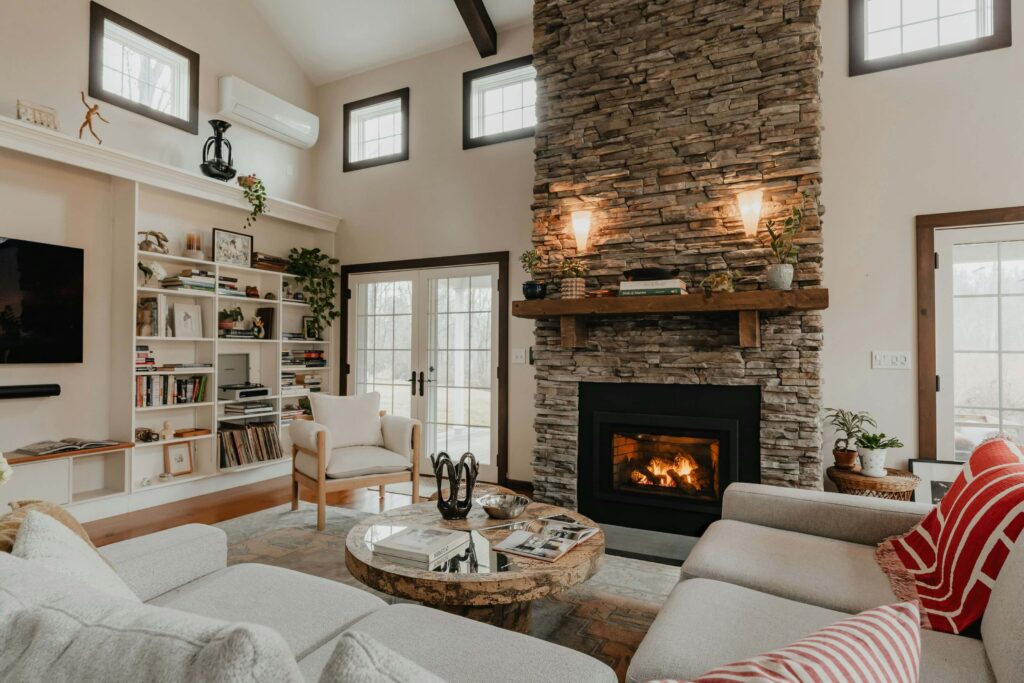 cozy white living room with tall stone fireplace focal point, white furniture, and a built-in bookcase