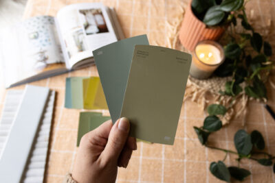 Hand holding two green paint samples over an orange tablecloth